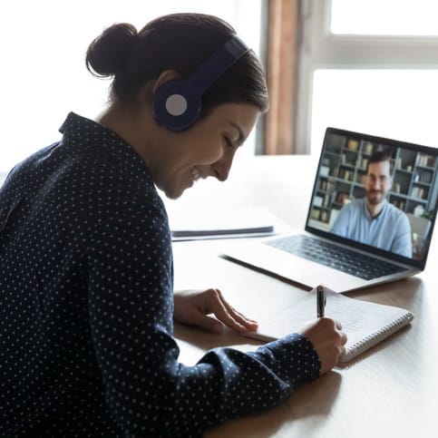 Woman wearing headphones and taking notes on a virtual call