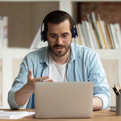 Serious man in glasses headphones sit at workplace desk talks through videoconference, take part in online stream communication use laptop, lead business negotiations remotely. Videocall event concept